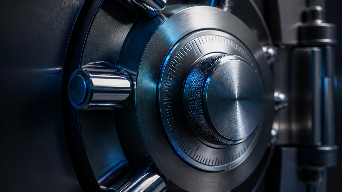 Brushed-steel bank vault combination dial and locking bolts in cool blue light, no people. Hire CISO