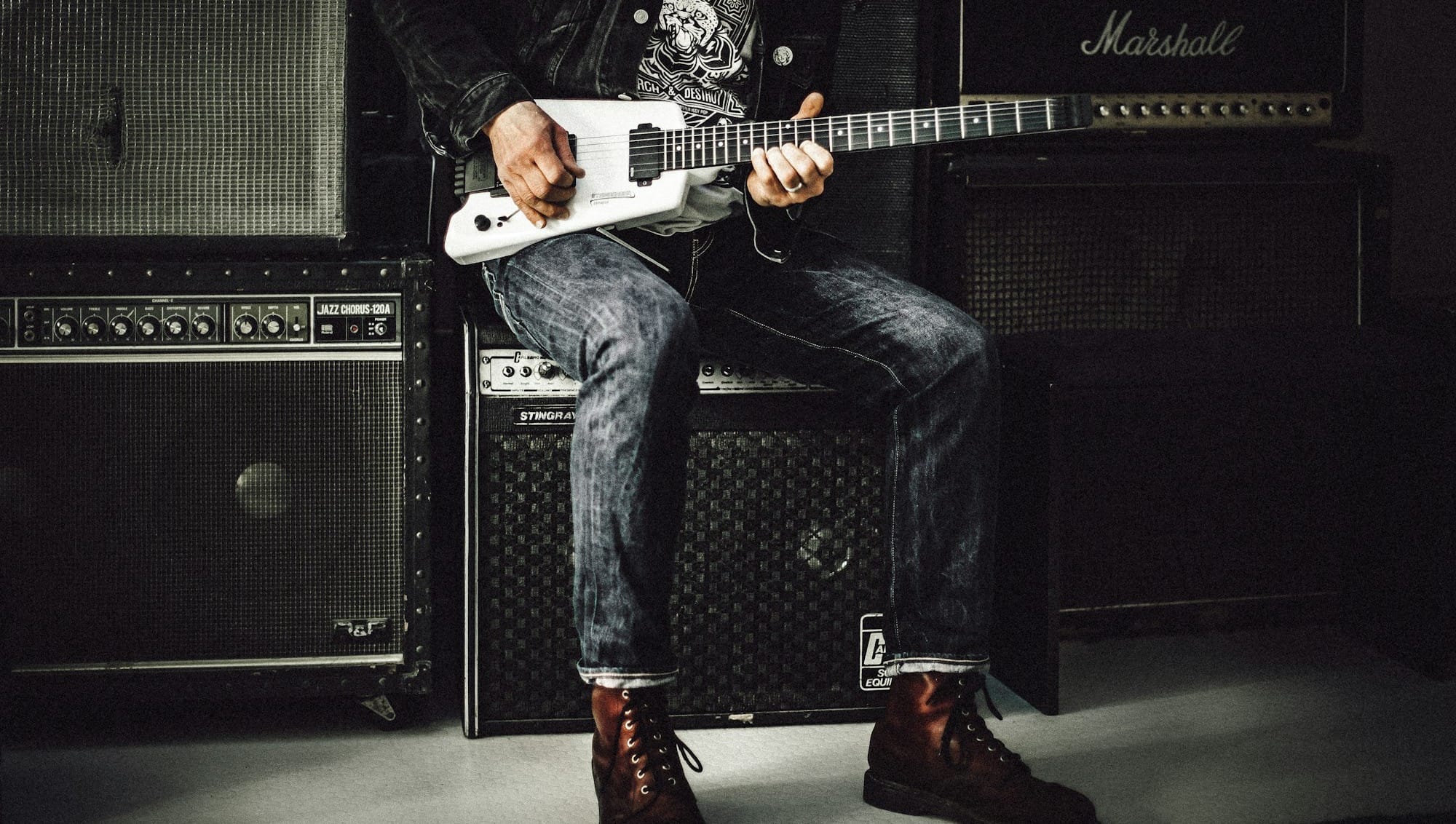 man wearing blue denim jeans playing white and black electric guitar sitting on black guitar amplifier