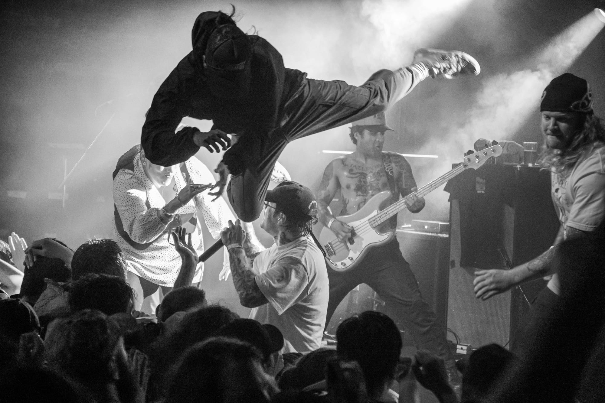 Hardcore metal band Angel Du$t performing on stage as crowd members stage dive into the crowd. Man is flying through the air with one leg out