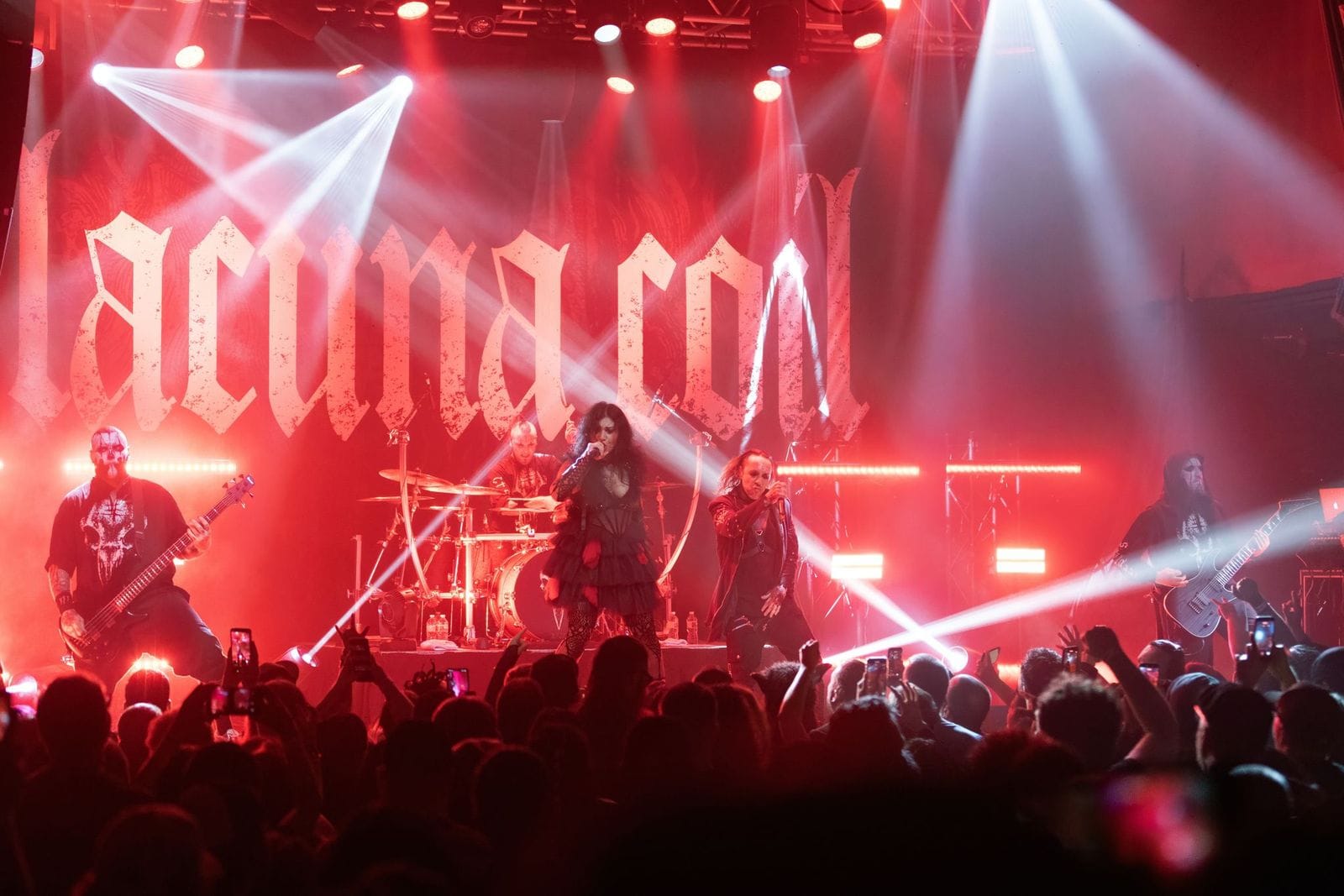 Lacuna Coil Concert Photos and Review: Lacuna Coil standing onstage performing as flashing lights and a red background are seen
