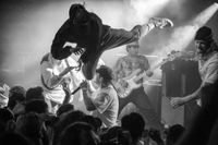 Hardcore metal band Angel Du$t performing on stage as crowd members stage dive into the crowd. Man is flying through the air with one leg out