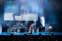 SatchVai Band on stage performing with smoke and blue lights cast across the stage