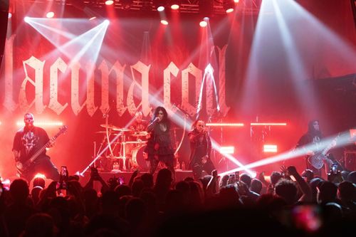 Lacuna Coil Concert Photos and Review: Lacuna Coil standing onstage performing as flashing lights and a red background are seen