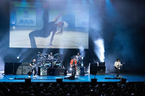 SatchVai Band on stage performing with smoke and blue lights cast across the stage