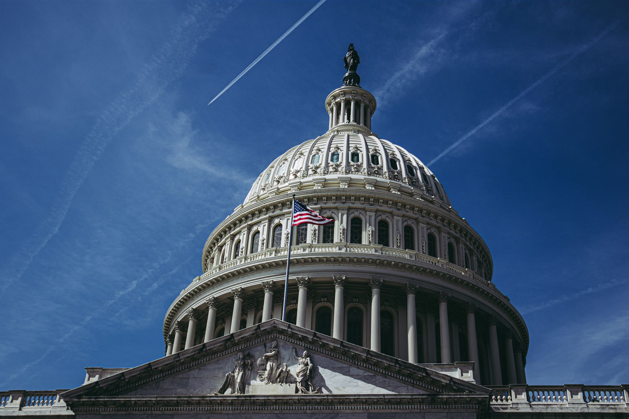 The dome of the US Capitol Building from outside, with an American flag out front.