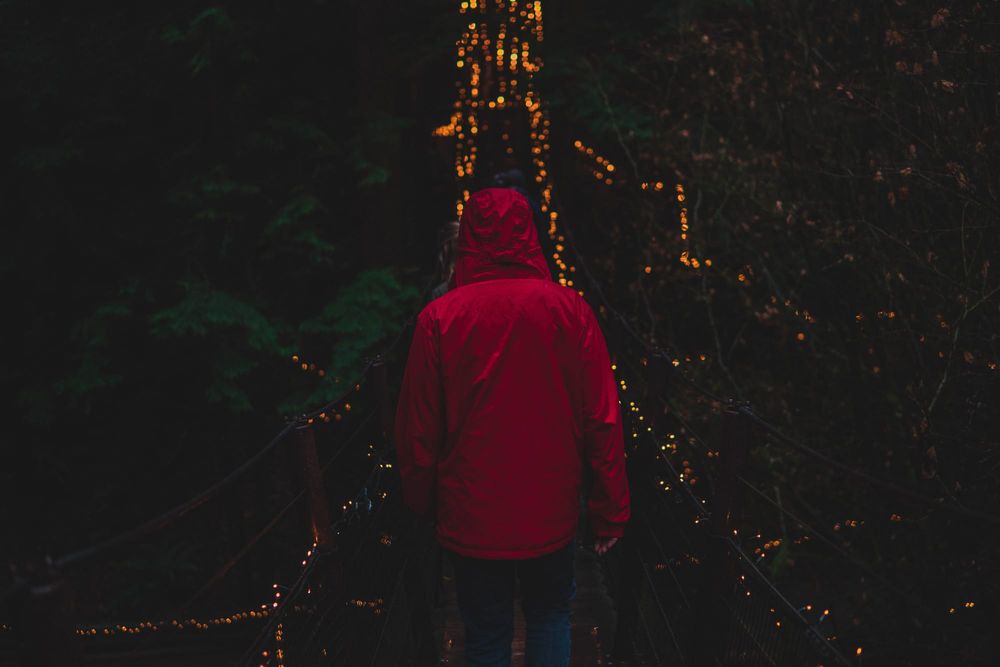 Man in red jacket crosses bridge with lights.