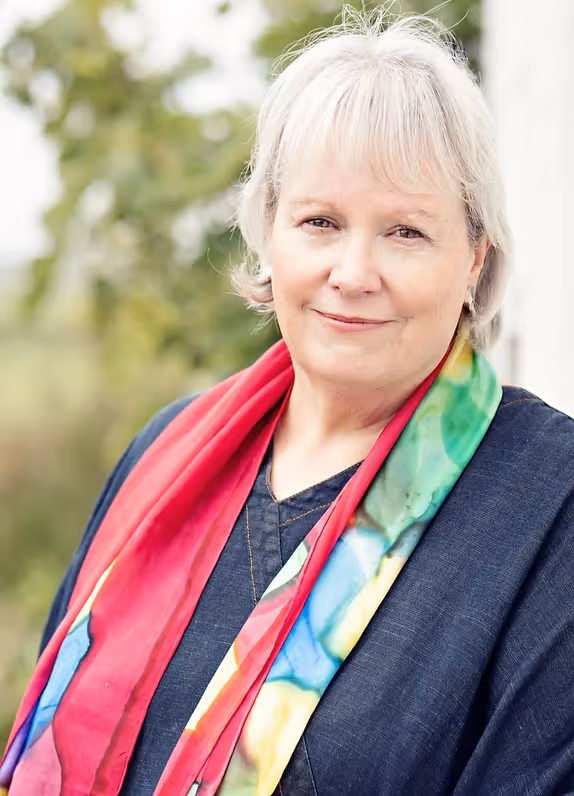 Author Lin Le Versha. Wearing a colorful scarf and denim shirt. Short light hair, smiling at the camera.