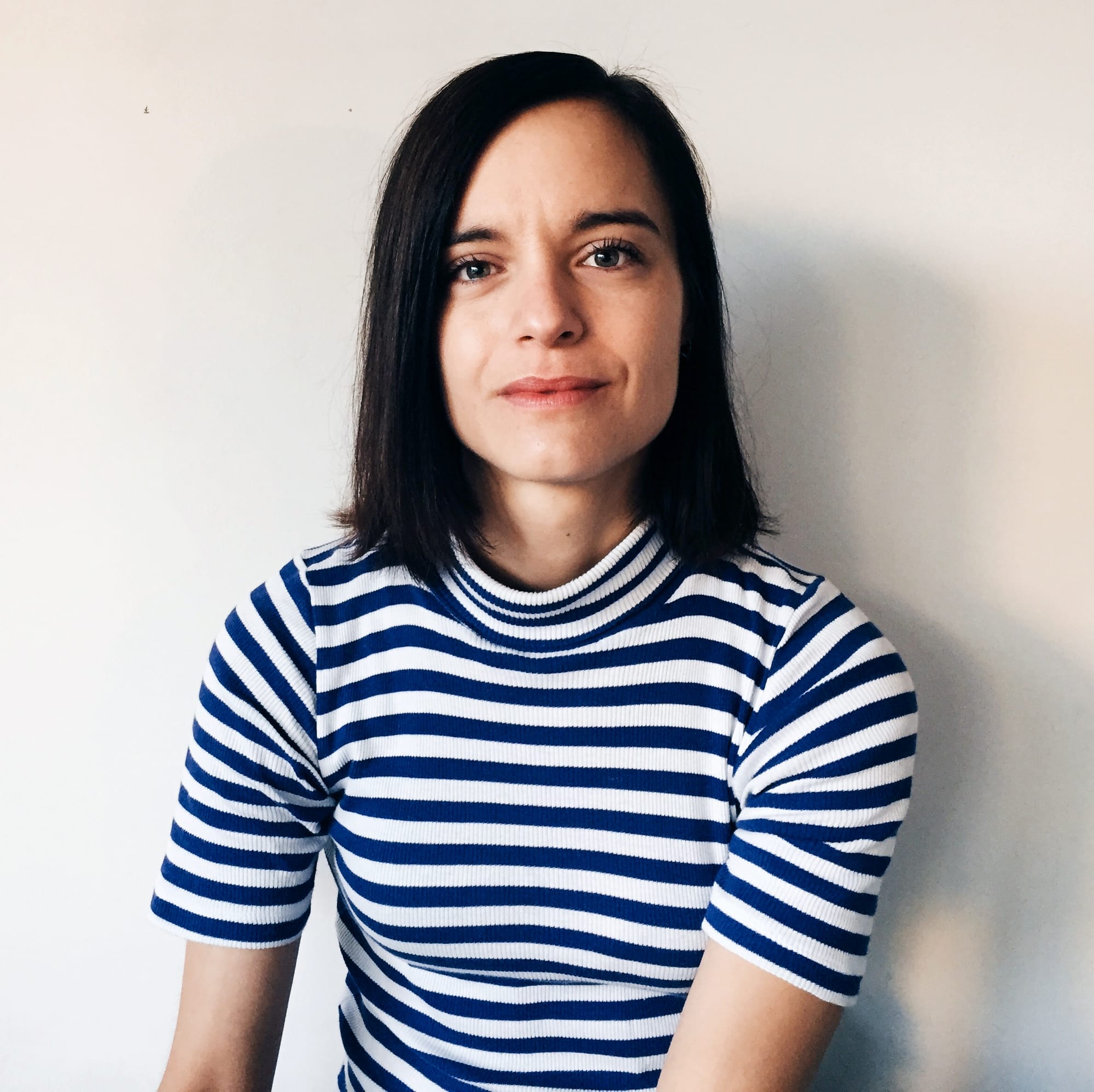 Author Jenny Lund Madsen in a blue and white striped short-sleeved shirt. Dark hair. Enigmatic smile. 