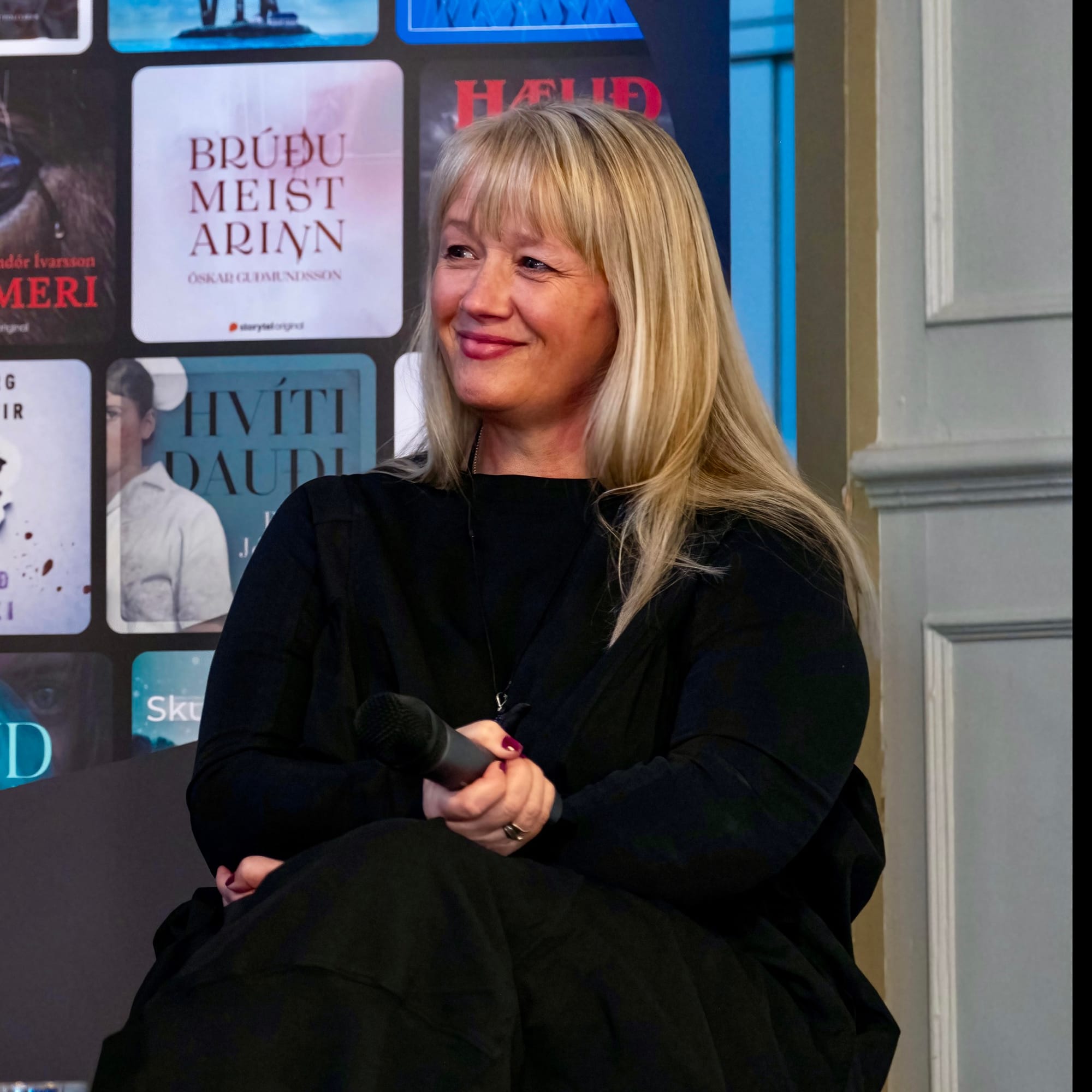 Author Suzy Aspley. Long blonde hair, smiling face, holding a microphone and dressed in black.