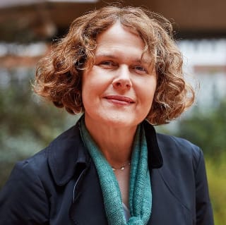 Author Kate Rhodes wearing a green scarf and navy blue jacket. She has curly brown hair and is smiling.