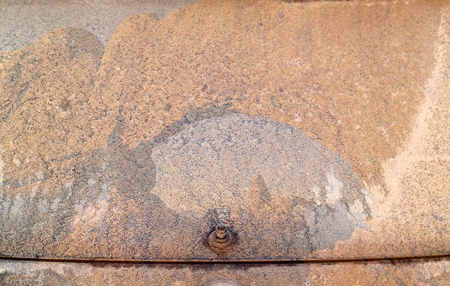 A desert landscape with sandstone arch is seen overlaid on the salt-crusted rear window of a hatchback automobile.