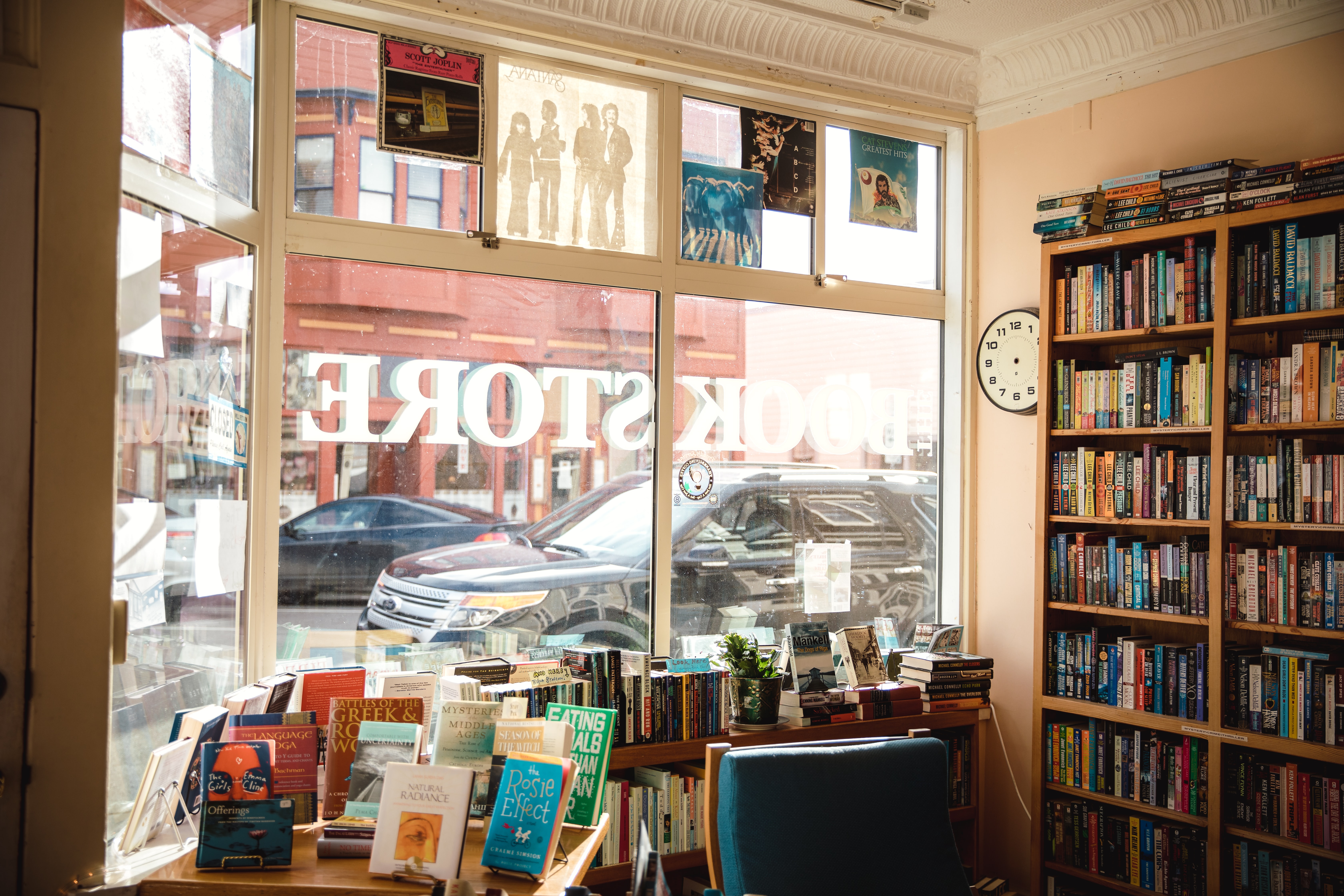 View from inside a small independent bookstore, looking past book displays out the front window onto a city street.