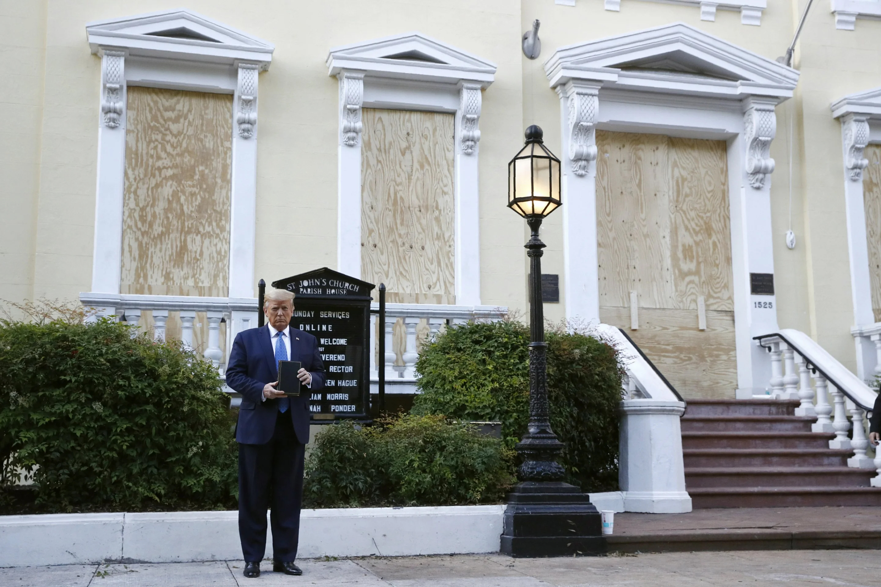 AP photo of Donald Trump standing awkwardly in front of the boarded-up windows of St. John's Church, holding a black Bible awkwardly in his tiny hands.