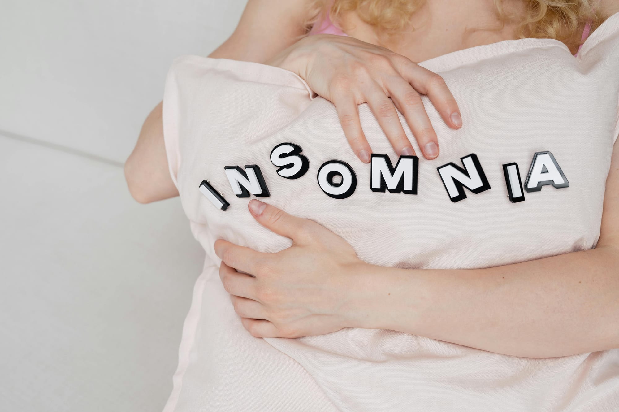 A women holding a pillow which reads "insomnia"