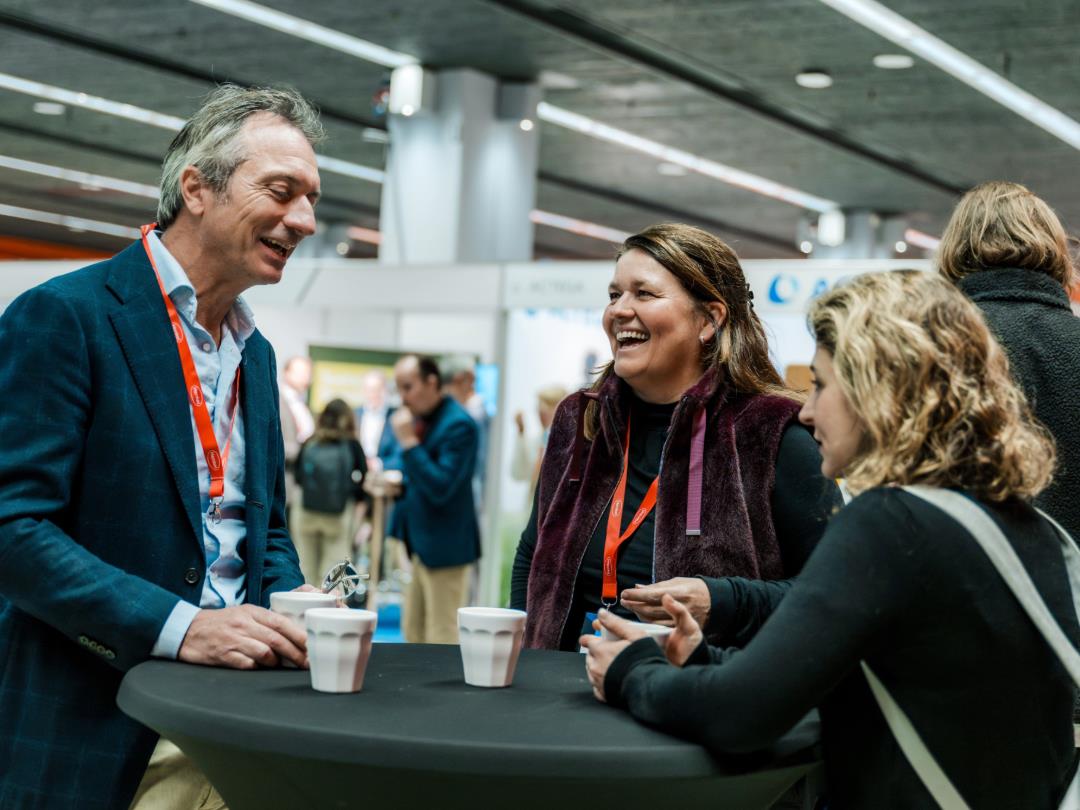 Three Sustainable Packaging Summit delegates talking around a table - two are stood up and one is sat down