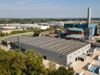 The new R3GID Aliplast plant in Modena, Italy. A rectangular grey building with solar panels on the roof and the blue and red Aliplast logo visible on the side of the building.