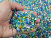 A pile of colourful polymer pellets viewed from above. A hand has scooped up some of the flakes and is holding them up…