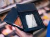 A hand is holding two plastic food trays containing breaded meat and an uncooked pastry. Each tray is lidded with a…