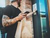 A delivery man holds a paper bag up to the camera. He appears to be ringing a doorbell at an apartment block, although this…
