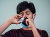 A man has tucked his medical face mask under his chin to access his nose. Pressing down on his left nostril, he has…