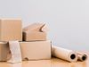 A pile of cardboard boxes, a paper bag, and rolls of paper wrapping are all displayed on a wooden surface.