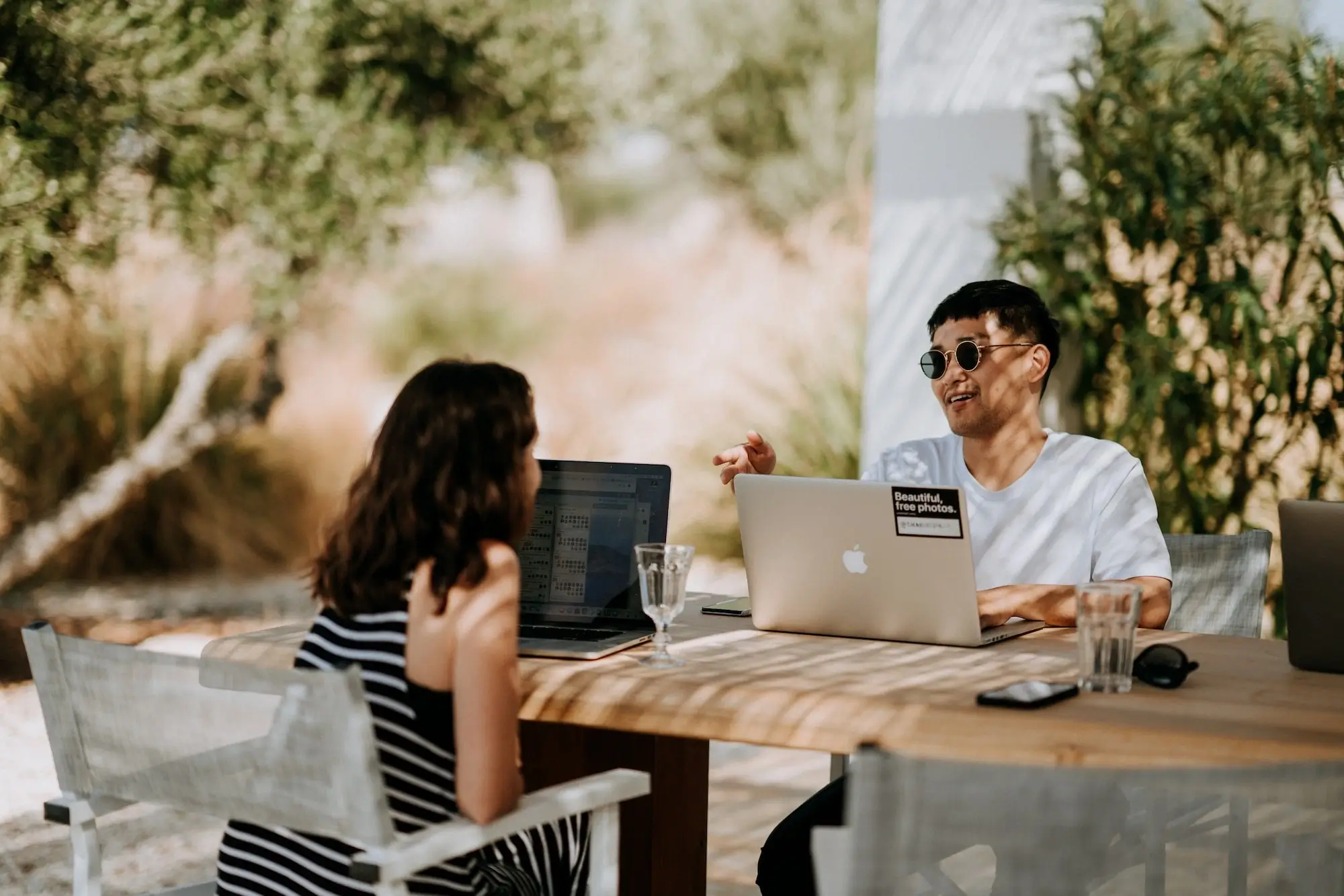 Zwei Softwareentwickler sitzen im Sommer draußen mit ihren Laptops vor sich und unterhalten sich