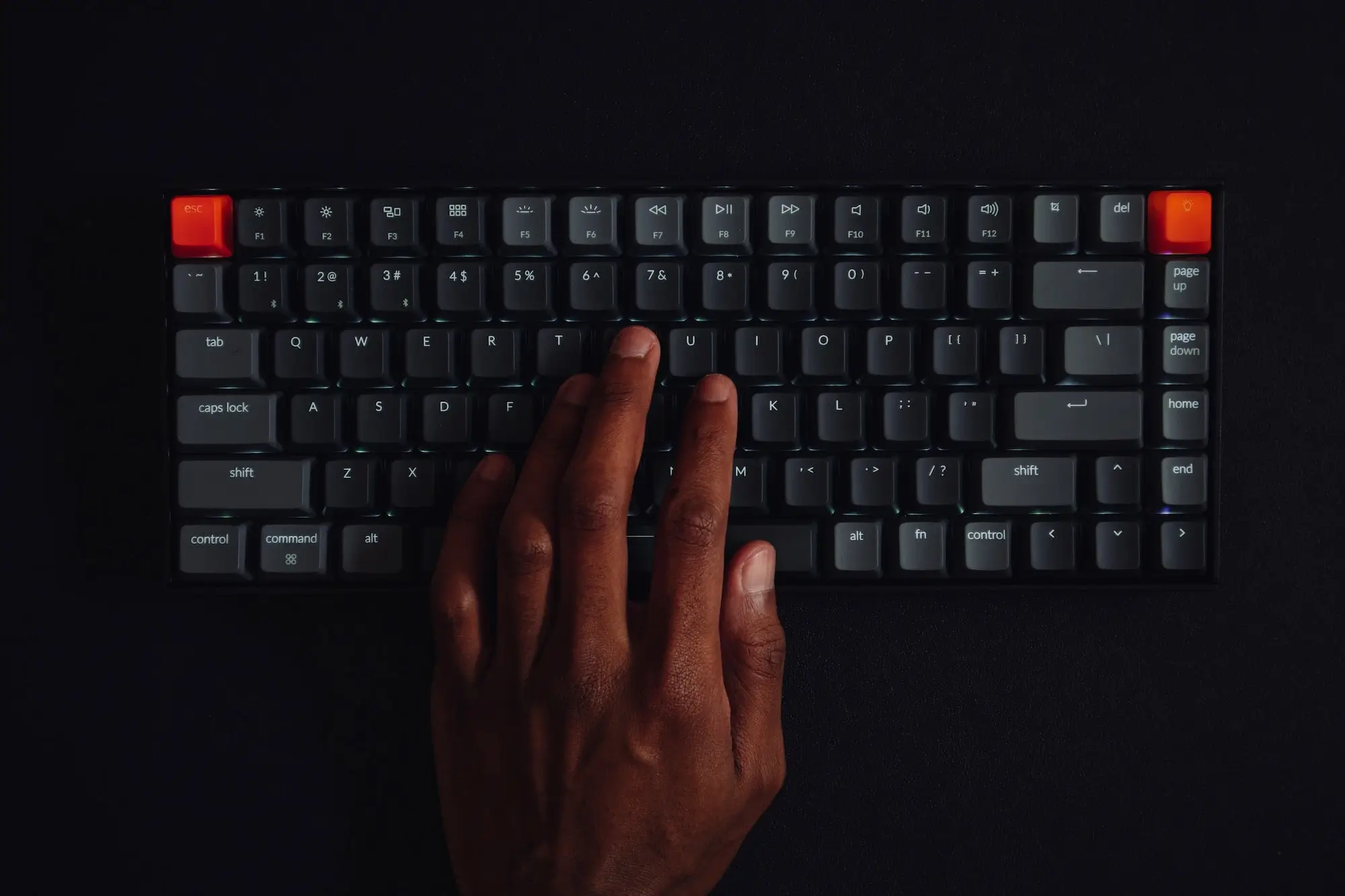 Hand auf einer schwarzen Tastatur mit zwei leuchtend roten Tasten oben links und rechts