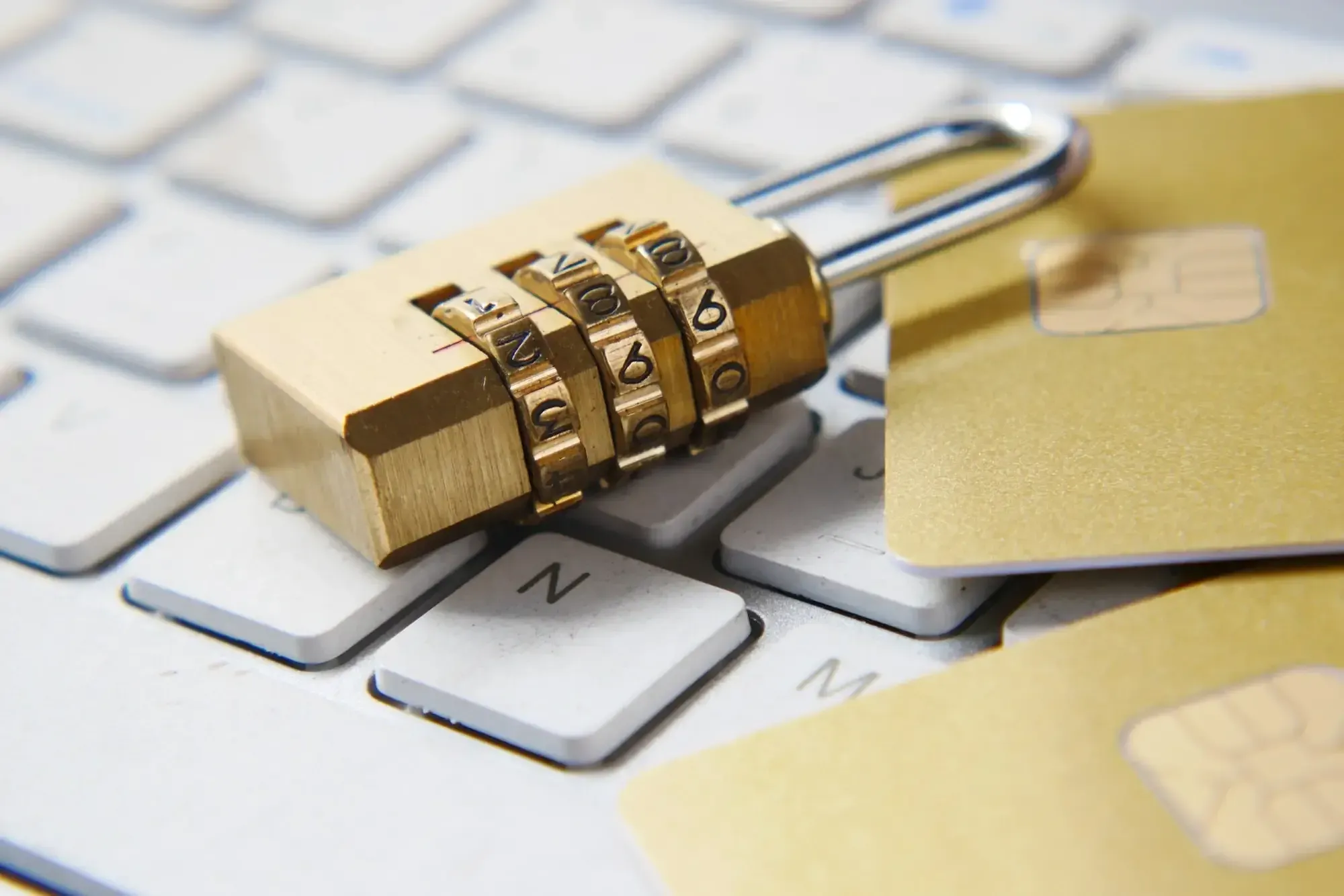Golden combination lock laying on white keyboard next to two golden chip cards.