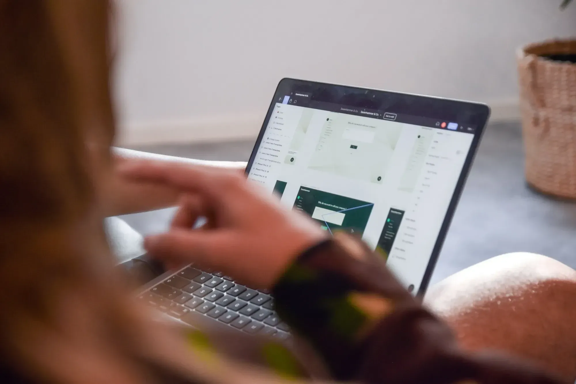 Laptop seitlich, Figma geöffnet, Personen im Vordergrund und Pflanze im Hintergrund unscharf.