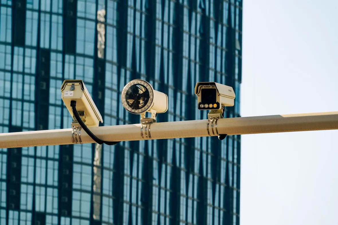 Surveillance cameras mounted along a gantry outside a glass office tower, the business CCTV that brings recording and retention duties.