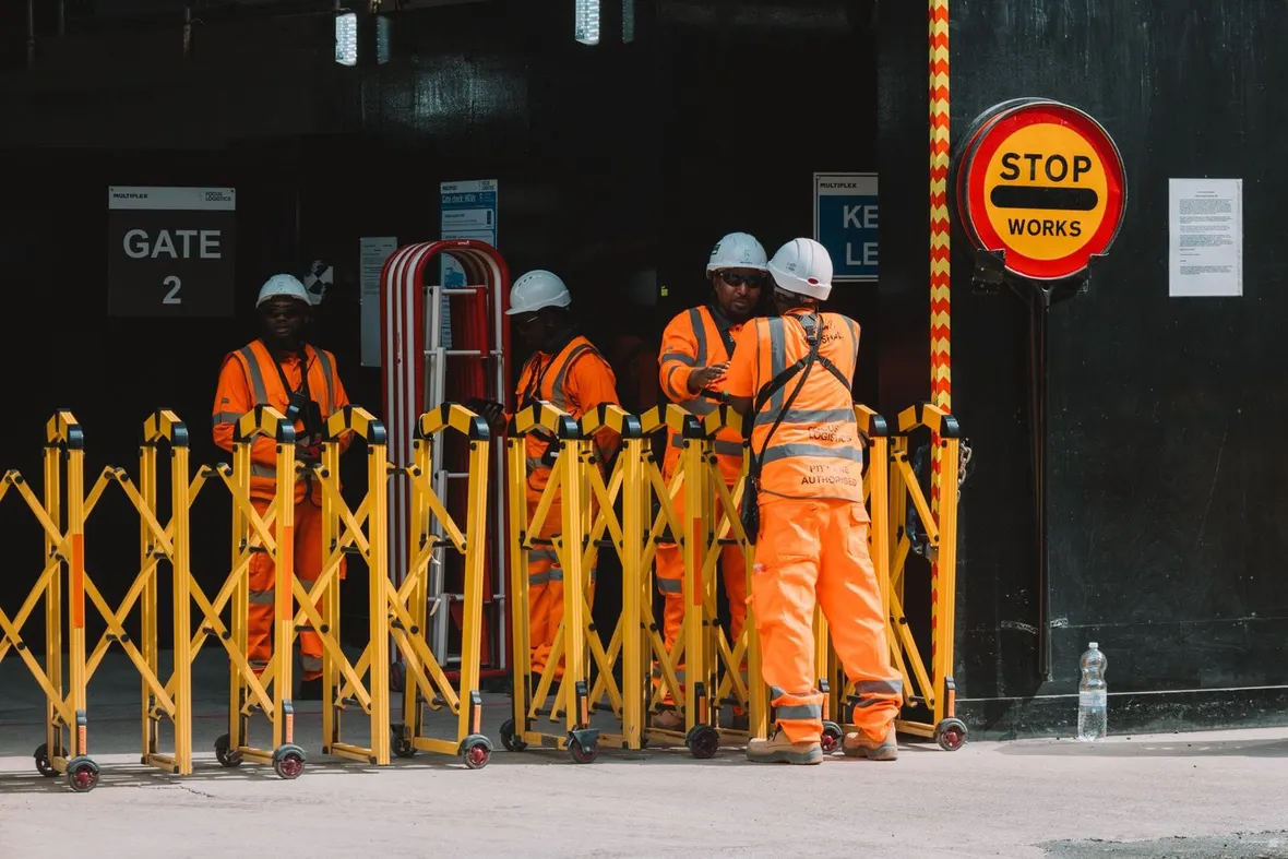 Workers in orange hi-vis and hard hats at a controlled construction site gate, the setting a pre-construction information pack covers.