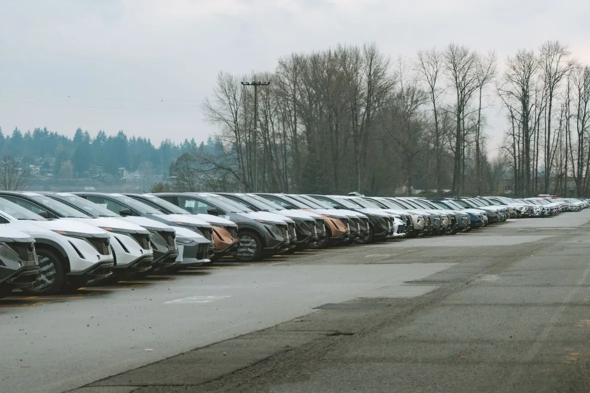 A long row of new cars parked nose out across a large tarmac compound, the kind of stock worth a finance check.