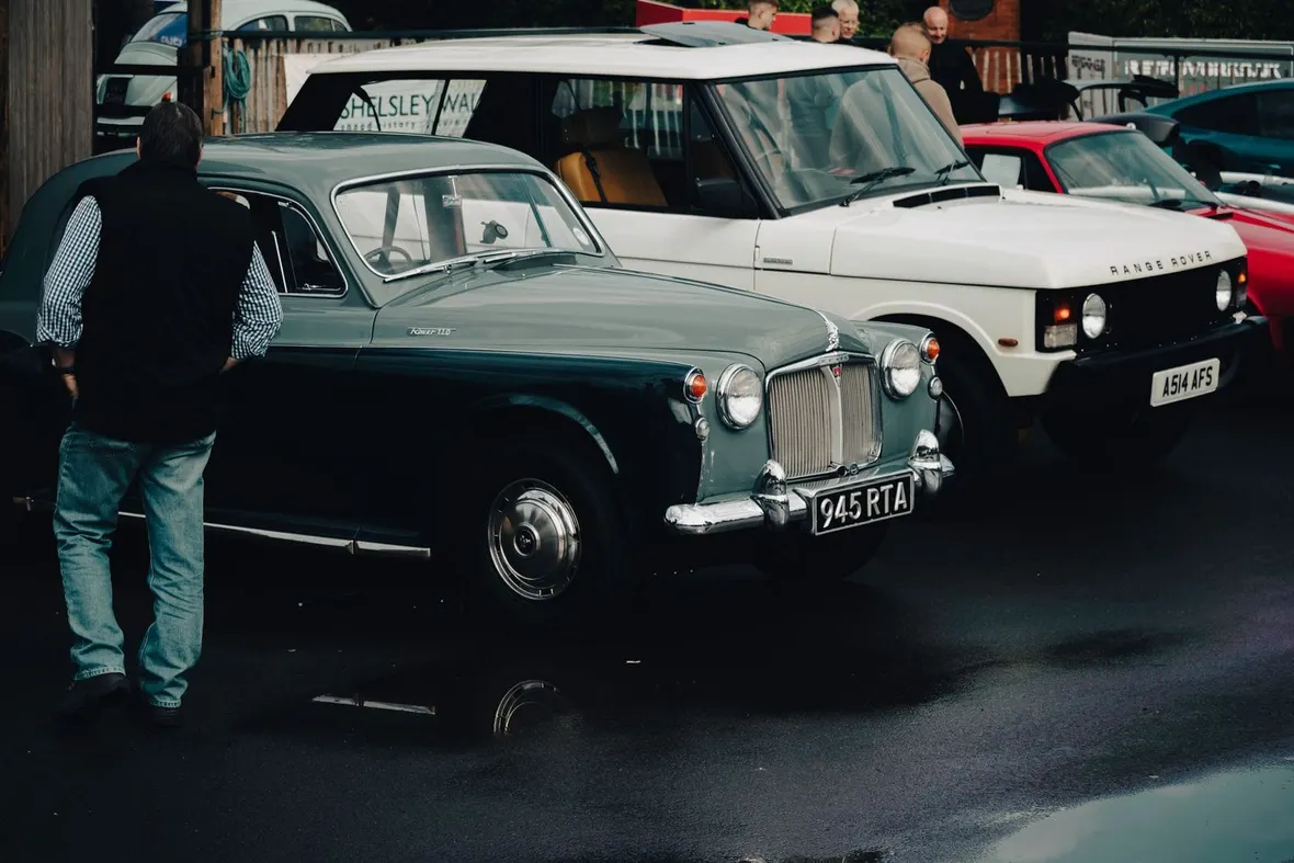 A dark green Rover 110 and white classic Range Rover at a UK gathering on period plates, the provenance a history file should record.