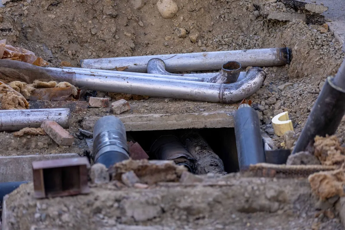 Exposed pipework in an unsupported excavation with loose earth sides, the kind of trench that needs a recorded inspection before work.