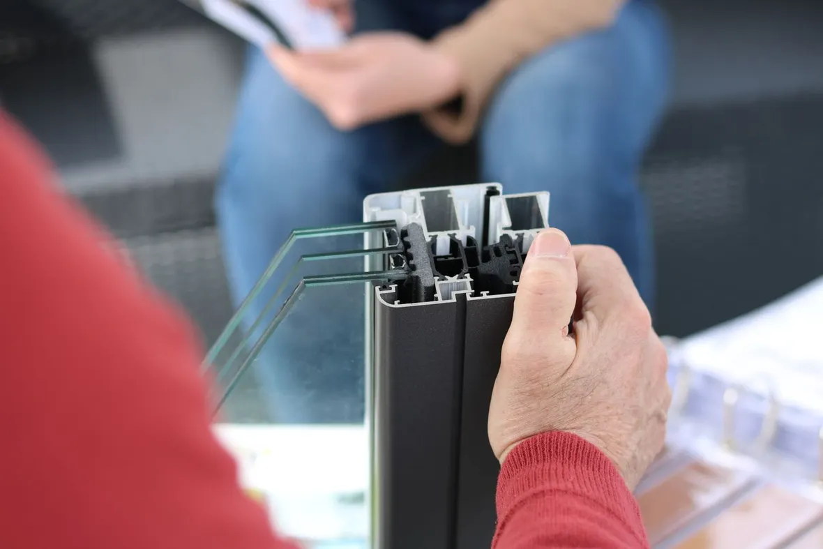 A hand holding a cutaway section of a double-glazed window frame and sealed unit, the replacement glazing a FENSA certificate covers.