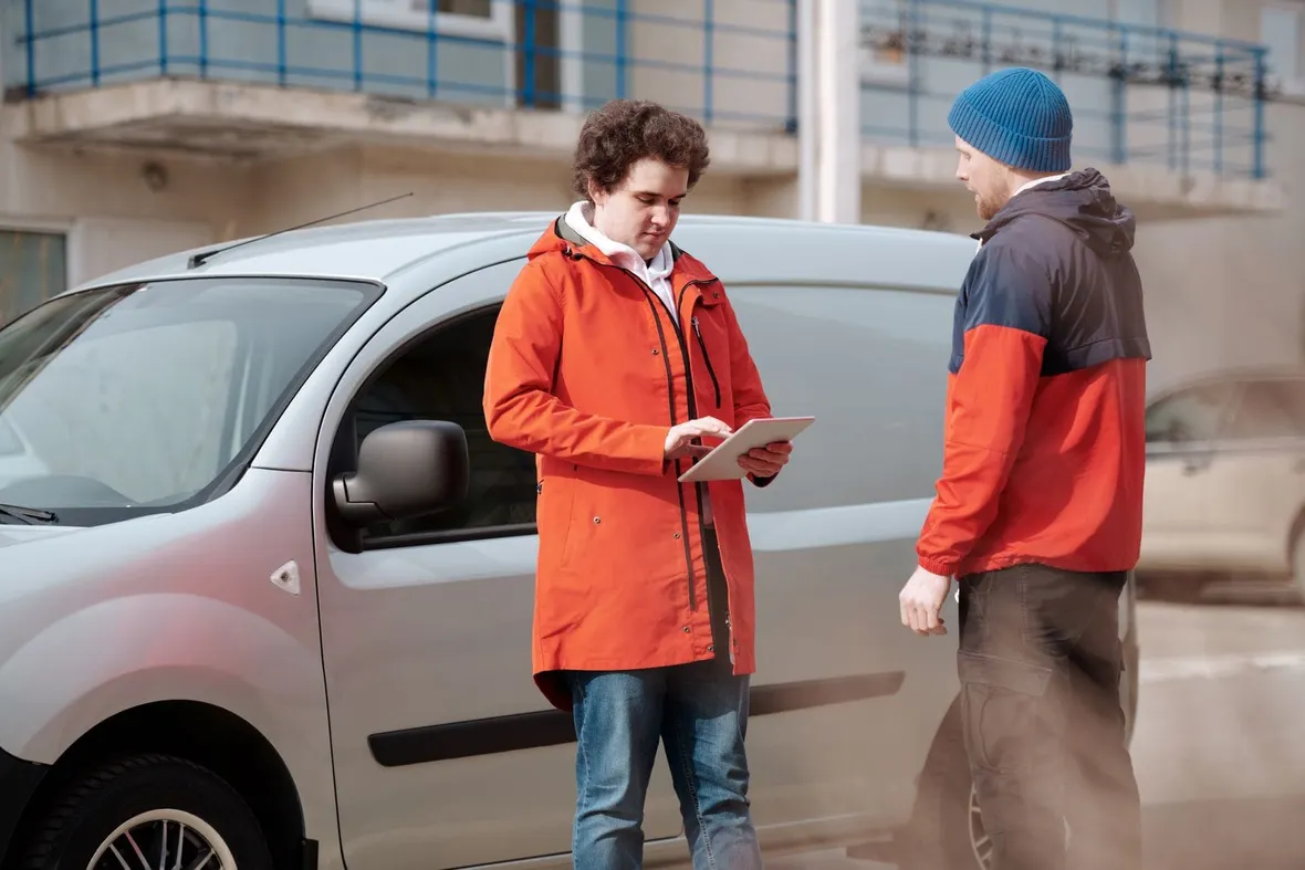Two men standing beside a silver van while one checks details on a tablet, comparing what free and paid car history checks reveal.