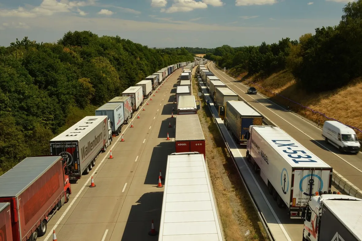 Articulated lorries queued in coned-off lanes on a UK motorway, the driving time HGV drivers must record on a tachograph.