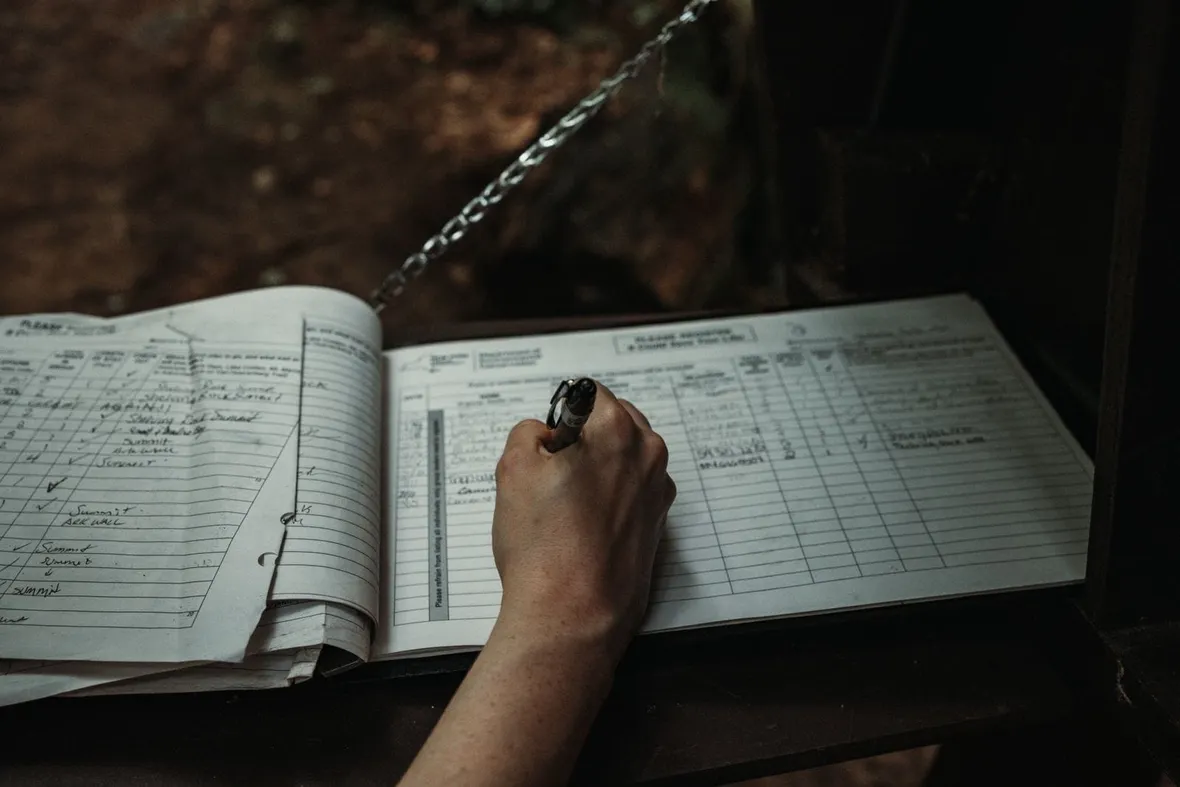 A hand writing entries in a ruled paper register with a pen, the same discipline a flight logbook needs.