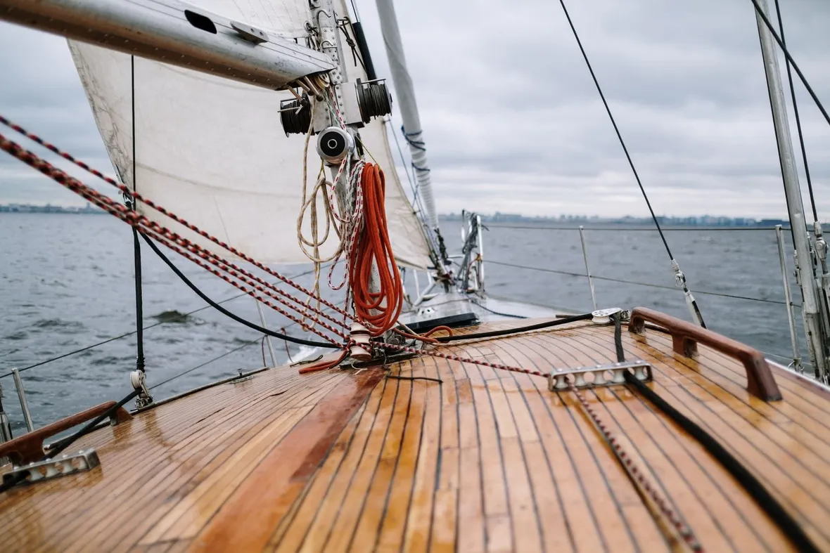 Varnished wooden foredeck and white sails of a yacht on grey open water, where each passage entry belongs in the logbook.