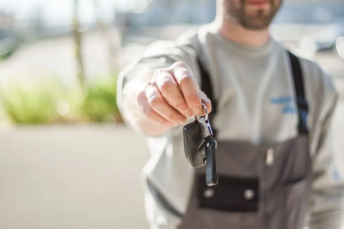 A man in workwear holding out a car key, the moment of handover when V5C ownership details must be transferred.