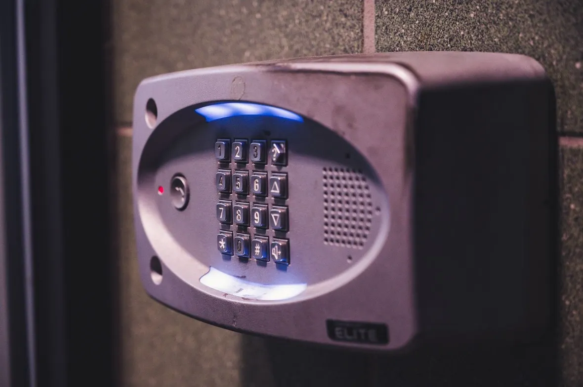 A backlit security keypad mounted on an exterior wall, the kind of alarm equipment a business logbook records tests and activations for.