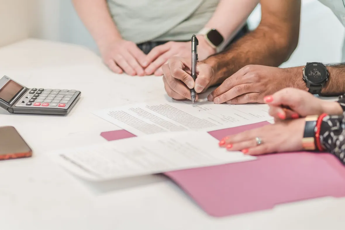 Hands signing printed paperwork beside a folding pocket calculator, the sort of agreement compared when weighing logbook loans against personal loans.