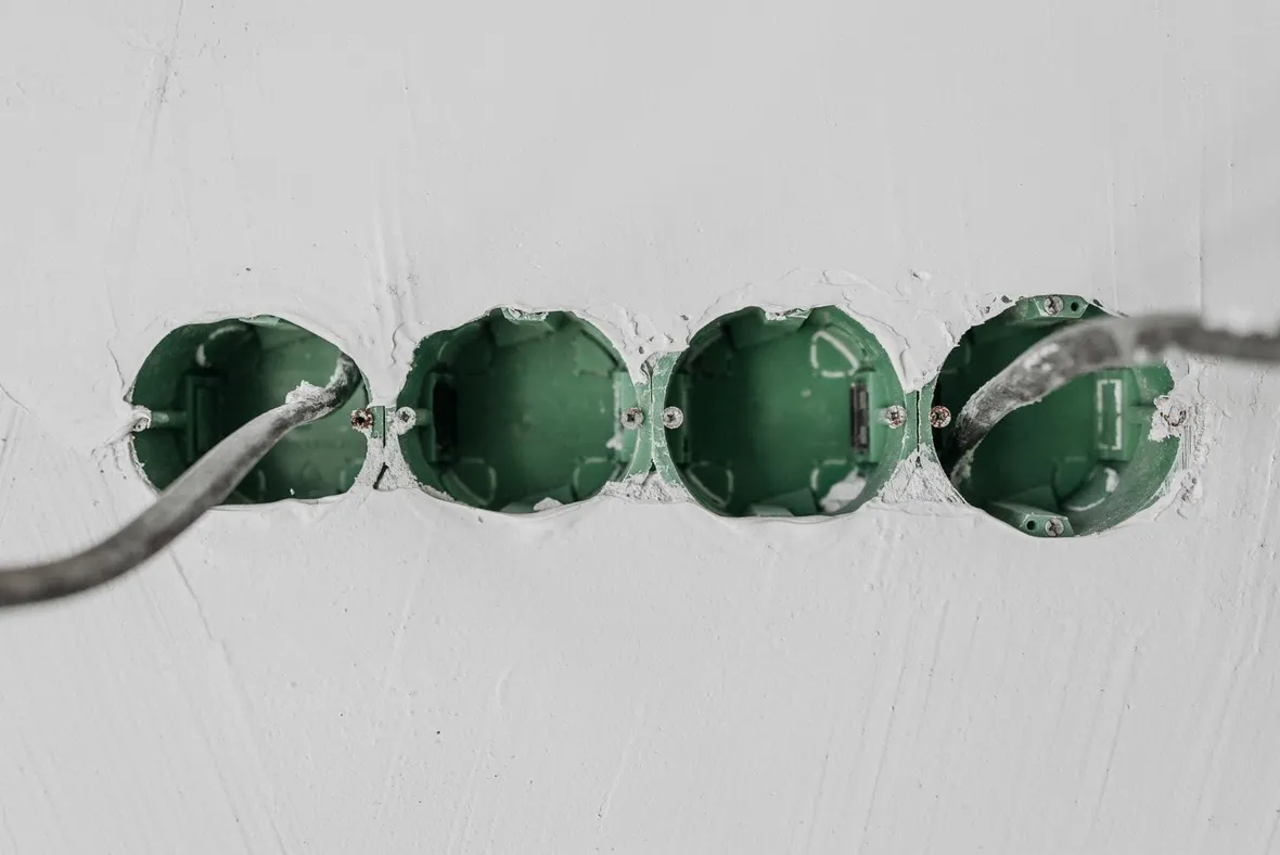 Grey cable feeding green plastic socket back boxes set into a plastered wall, the domestic electrical work Part P certificates record.