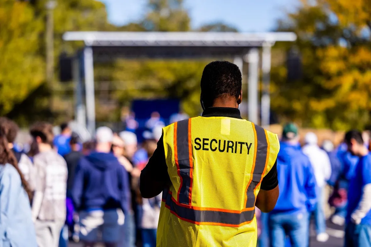 A security steward in a yellow hi-vis vest facing a crowd at an outdoor event, the kind of shift a duty log records.