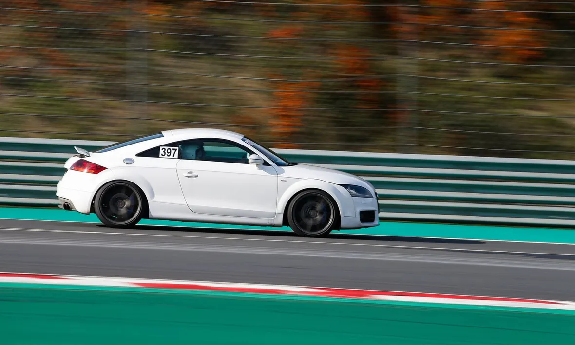 White sports coupe with a taped-on number board cornering on a race circuit, the kind of session drivers should log.