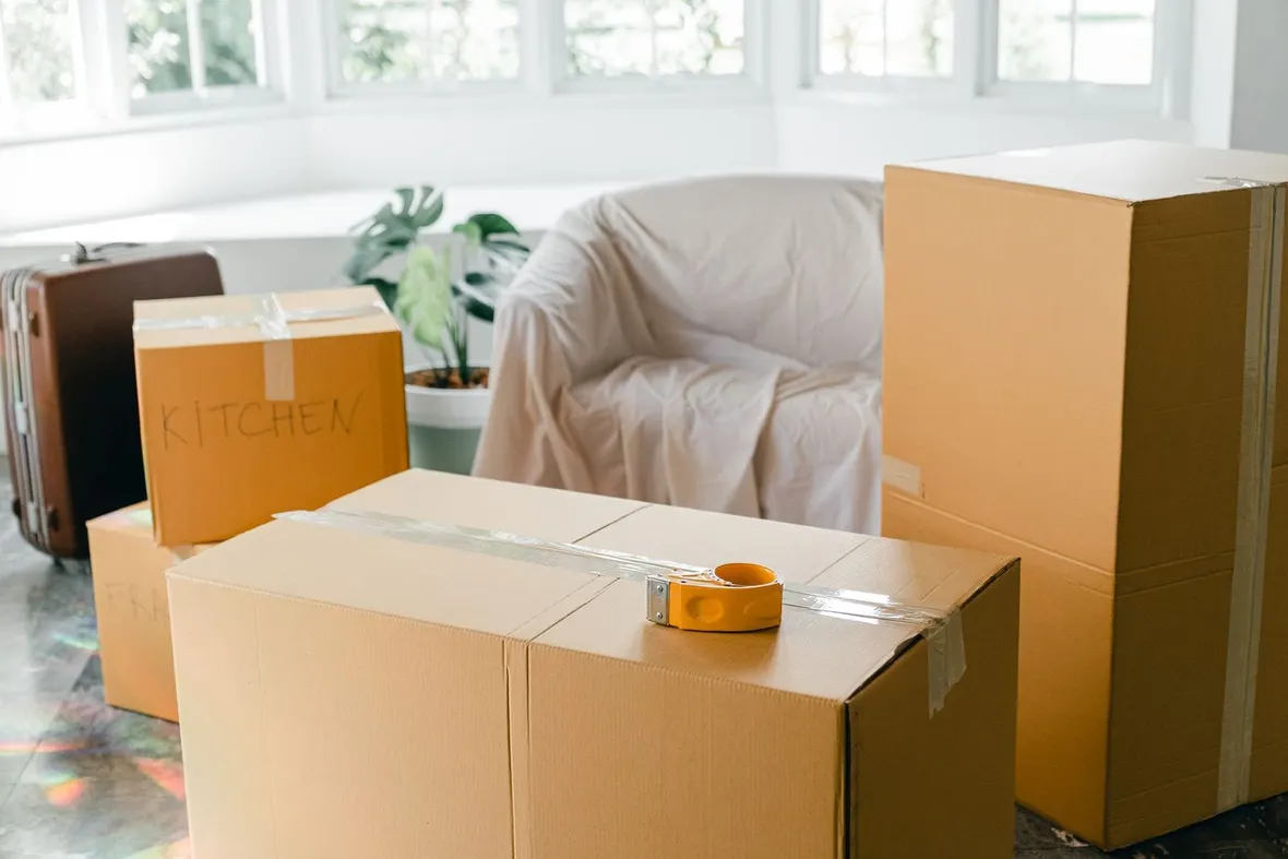 Cardboard packing boxes labelled by room with a tape gun and dust sheet, the house move that triggers a V5C address change.