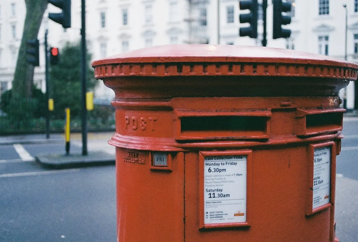 A red Royal Mail pillar box beside a London road junction, where a completed V62 application starts its journey to DVLA.