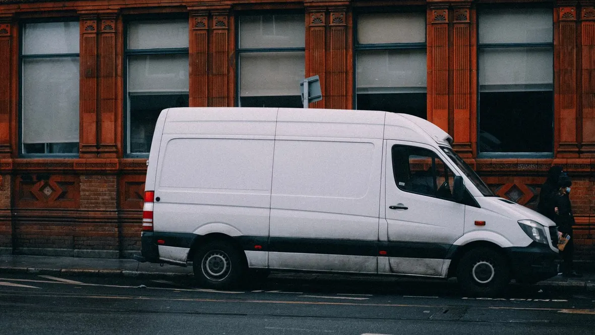 White panel van parked on a city street outside a red brick building, the everyday vehicle behind van driver record keeping.