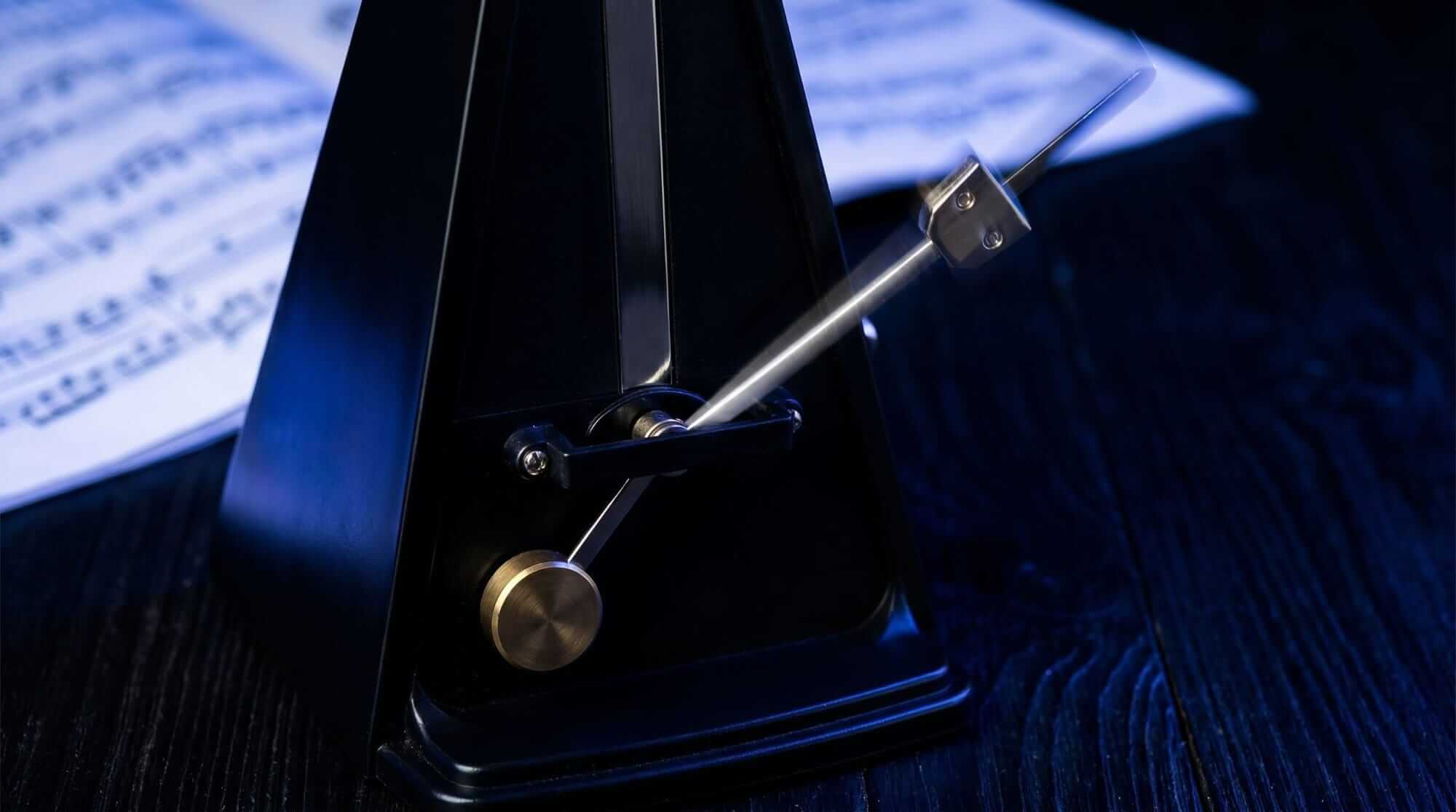Close-up of a mechanical metronome with sheet music in the background.