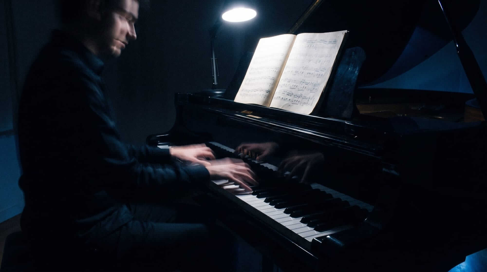 Pianist performing at a grand piano while reading sheet music in a dark studio setting.